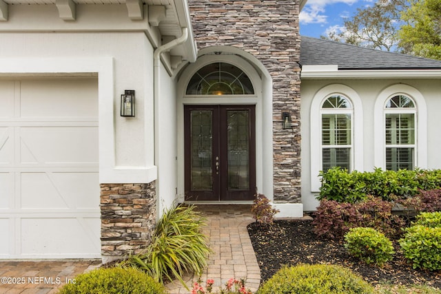 property entrance with a shingled roof, stucco siding, an attached garage, french doors, and stone siding