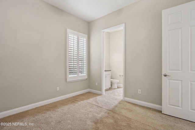 unfurnished bedroom featuring carpet, baseboards, multiple windows, and ensuite bathroom