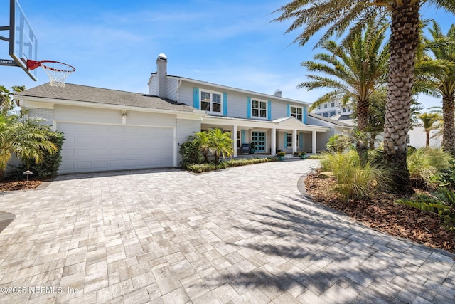 traditional home featuring a porch, a chimney, driveway, brick siding, and an attached garage