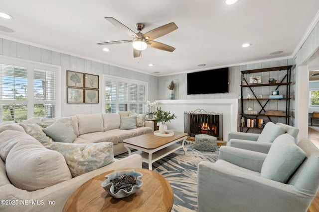 living room featuring a healthy amount of sunlight, a ceiling fan, ornamental molding, and a lit fireplace