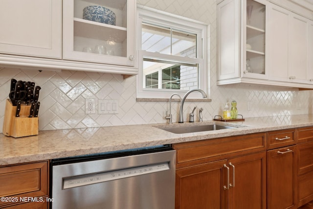 kitchen with light stone counters, stainless steel dishwasher, white cabinets, glass insert cabinets, and a sink