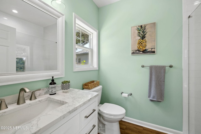 full bathroom with a tile shower, baseboards, toilet, wood finished floors, and vanity