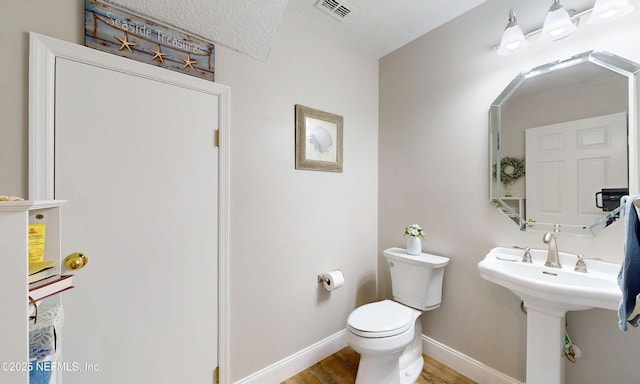 bathroom with baseboards, toilet, wood finished floors, and visible vents