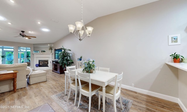 dining space with vaulted ceiling, a glass covered fireplace, recessed lighting, light wood-style floors, and ceiling fan with notable chandelier