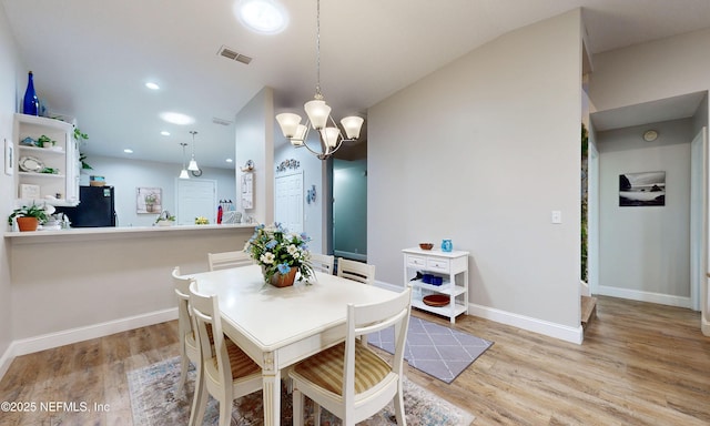 dining room featuring visible vents, light wood-style flooring, a chandelier, and vaulted ceiling