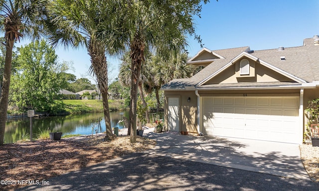 view of front facade featuring concrete driveway, a water view, a shingled roof, an attached garage, and stucco siding