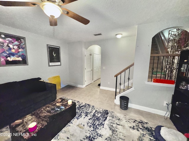 living room featuring a textured ceiling, ceiling fan, arched walkways, tile patterned flooring, and visible vents