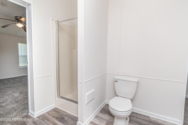 bathroom featuring a shower with door, wood finished floors, toilet, baseboards, and ceiling fan