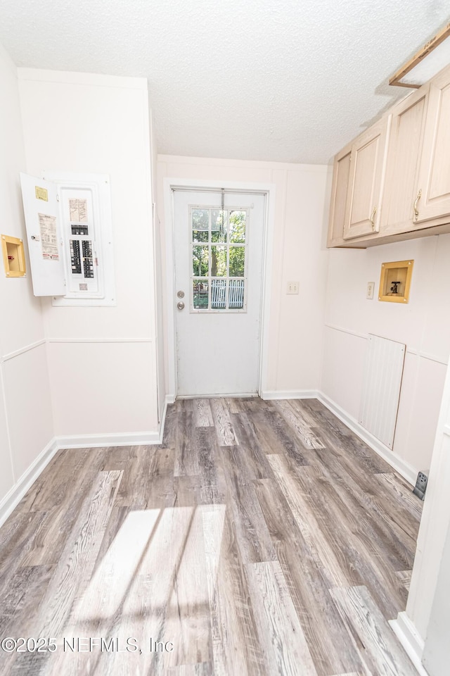 washroom featuring hookup for a washing machine, a textured ceiling, electric panel, light wood-type flooring, and cabinet space