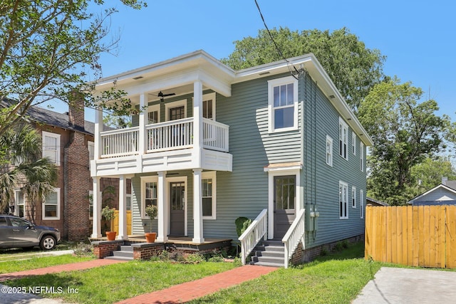 greek revival inspired property with a porch, fence, a ceiling fan, a balcony, and a front yard
