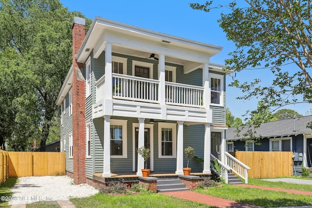 greek revival house with a porch, a chimney, a balcony, and fence