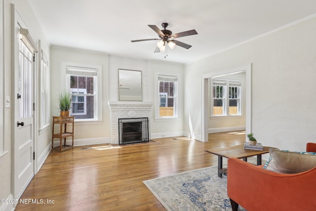 living room featuring a brick fireplace, wood finished floors, a wealth of natural light, and ceiling fan