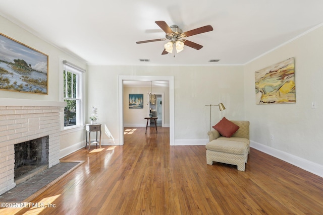 living area with wood finished floors, visible vents, baseboards, a brick fireplace, and ceiling fan