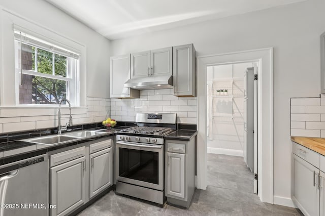kitchen featuring stainless steel appliances, a sink, dark countertops, gray cabinets, and under cabinet range hood