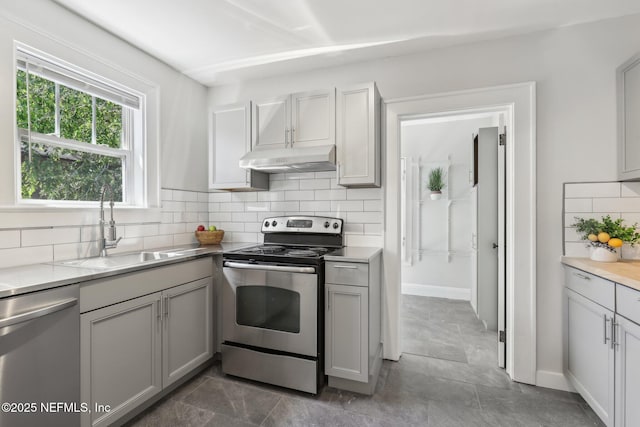 kitchen with under cabinet range hood, gray cabinets, a sink, decorative backsplash, and appliances with stainless steel finishes