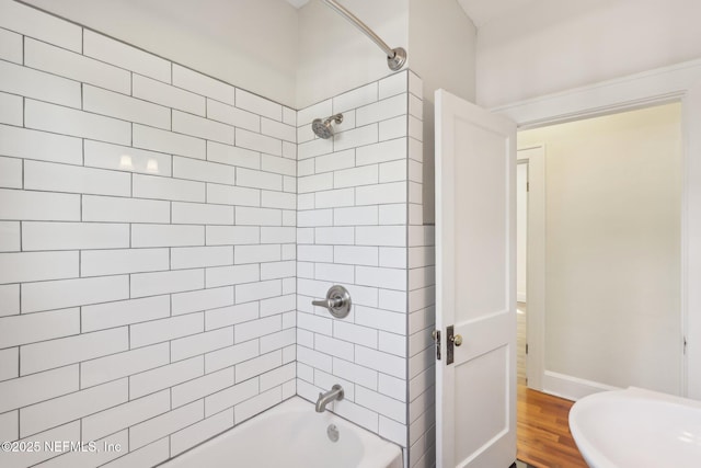 bathroom with baseboards, wood finished floors, and bathing tub / shower combination