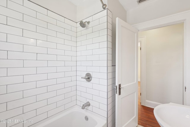 bathroom featuring baseboards, wood finished floors, and washtub / shower combination