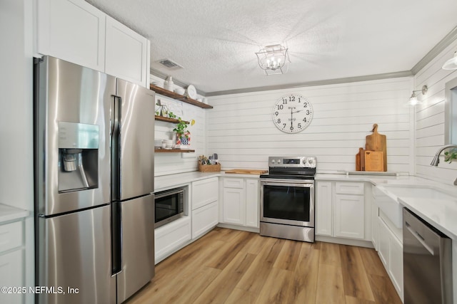 4068 Scenic Dr, Middleburg, FL 32068 - kitchen with white cabinets, light wood finished floors, stainless steel appliances, a sink, and a textured ceiling