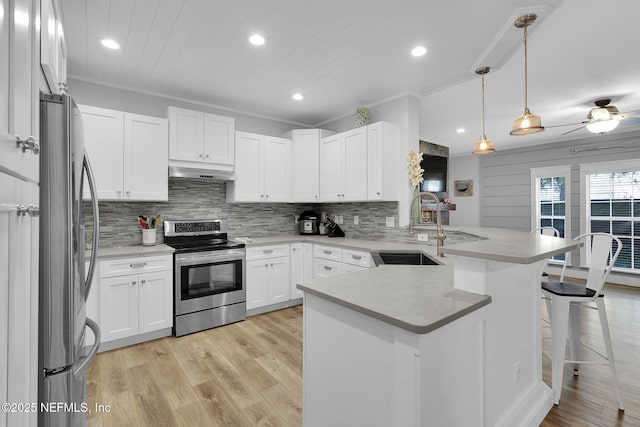 kitchen with a sink, under cabinet range hood, a peninsula, backsplash, and appliances with stainless steel finishes