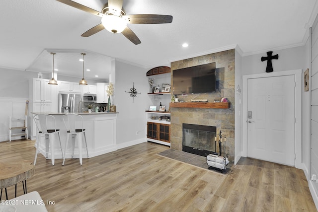 living area featuring ornamental molding, ceiling fan, a stone fireplace, and light wood-style flooring