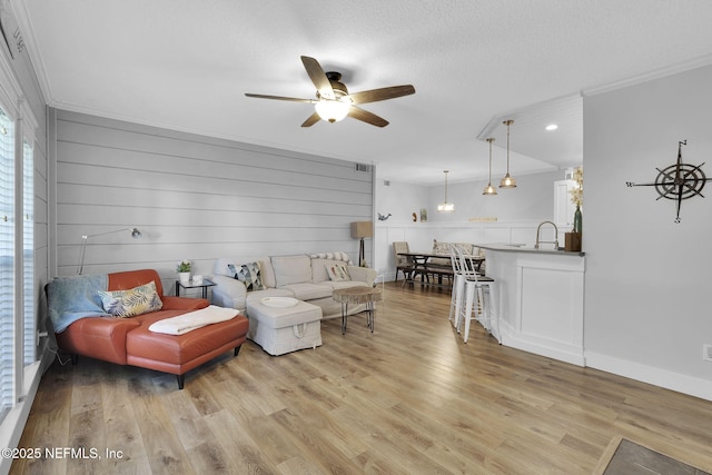 living room featuring light wood-style floors, a ceiling fan, visible vents, and crown molding