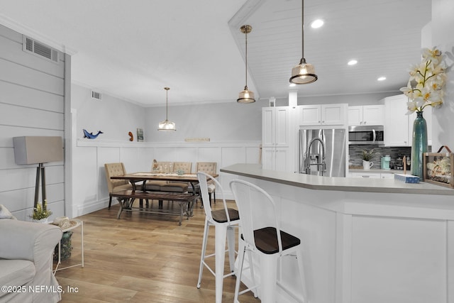 kitchen featuring white cabinets, appliances with stainless steel finishes, visible vents, light wood finished floors, and backsplash