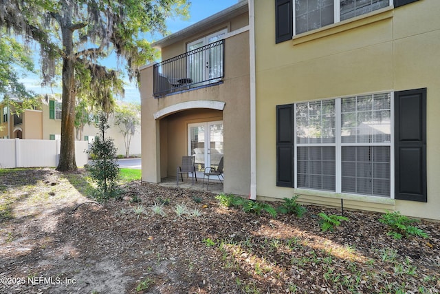 back of house featuring fence, french doors, a balcony, and stucco siding