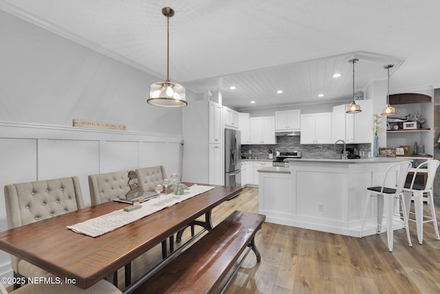 dining area featuring recessed lighting, a wainscoted wall, light wood-style floors, and crown molding