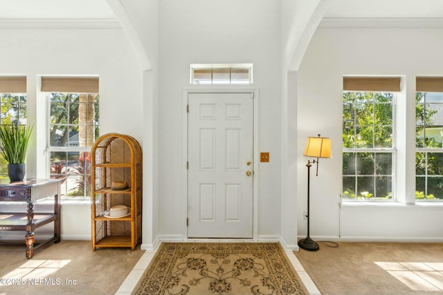 foyer with arched walkways, a healthy amount of sunlight, and light carpet