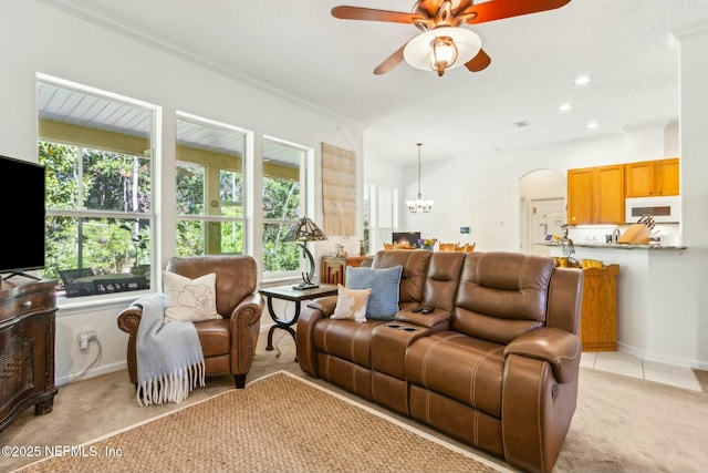living room featuring ceiling fan with notable chandelier, arched walkways, light carpet, ornamental molding, and recessed lighting