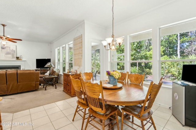 dining space featuring light tile patterned floors, crown molding, a fireplace, light colored carpet, and ceiling fan with notable chandelier