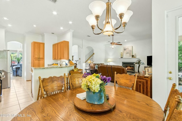 dining space with arched walkways, recessed lighting, ceiling fan with notable chandelier, a warm lit fireplace, and light tile patterned floors