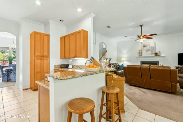 kitchen featuring open floor plan, light tile patterned floors, ceiling fan, arched walkways, and a peninsula
