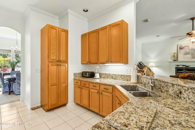 kitchen with light stone counters, a sink, ceiling fan with notable chandelier, light tile patterned floors, and arched walkways
