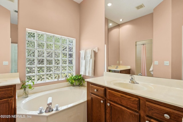 bathroom featuring a bath, two vanities, a sink, and visible vents