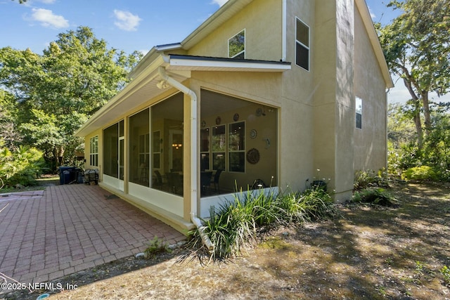 view of property exterior featuring stucco siding, a sunroom, and a patio