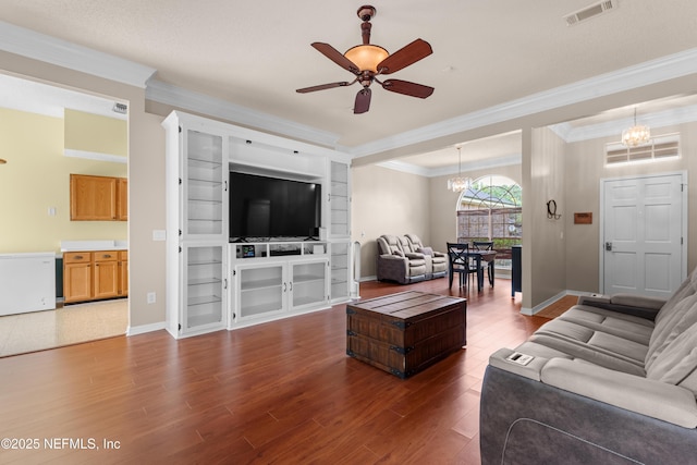 living area with crown molding, dark wood finished floors, ceiling fan with notable chandelier, baseboards, and visible vents