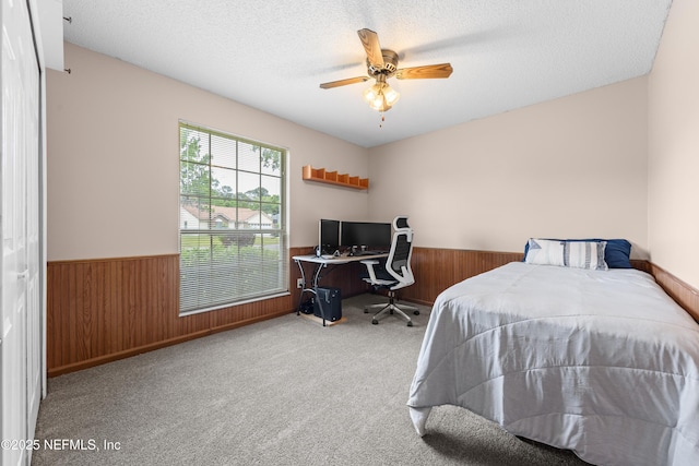 bedroom with carpet flooring, a textured ceiling, wood walls, and wainscoting