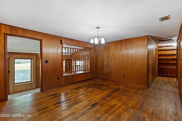 spare room featuring wood-type flooring, wooden walls, visible vents, and a notable chandelier