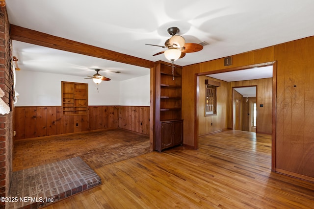 empty room with wood walls, a wainscoted wall, visible vents, a ceiling fan, and parquet floors