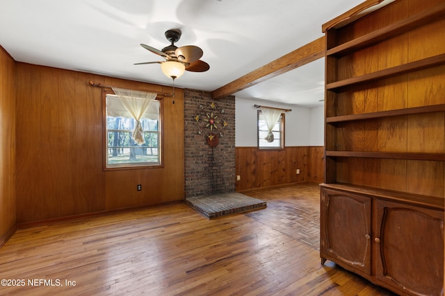 unfurnished living room with a ceiling fan, light wood-style floors, wooden walls, and plenty of natural light