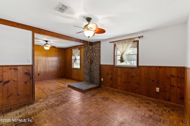 spare room with wainscoting, visible vents, beamed ceiling, a ceiling fan, and wood walls