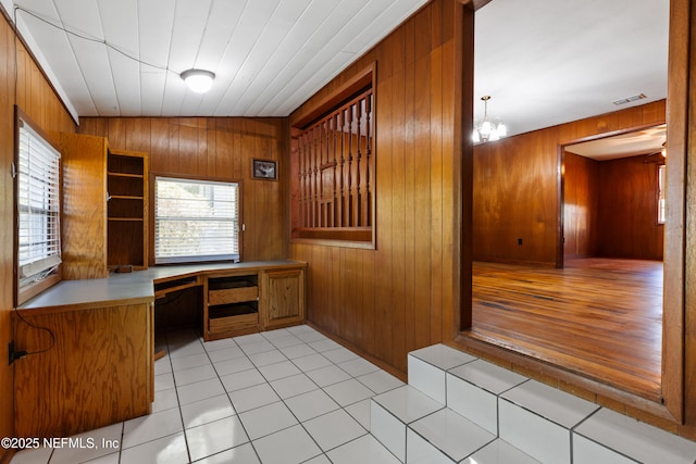 interior space with visible vents, an inviting chandelier, wood walls, built in study area, and light tile patterned floors