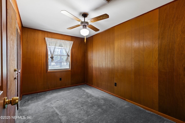 empty room featuring wood walls, a ceiling fan, and carpet flooring