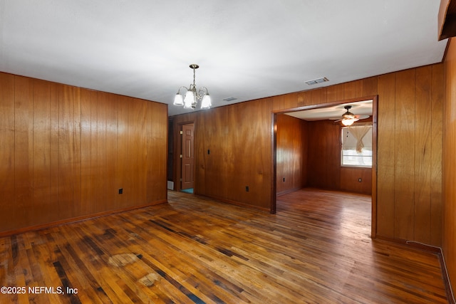 unfurnished room featuring wood walls, ceiling fan with notable chandelier, visible vents, and wood-type flooring