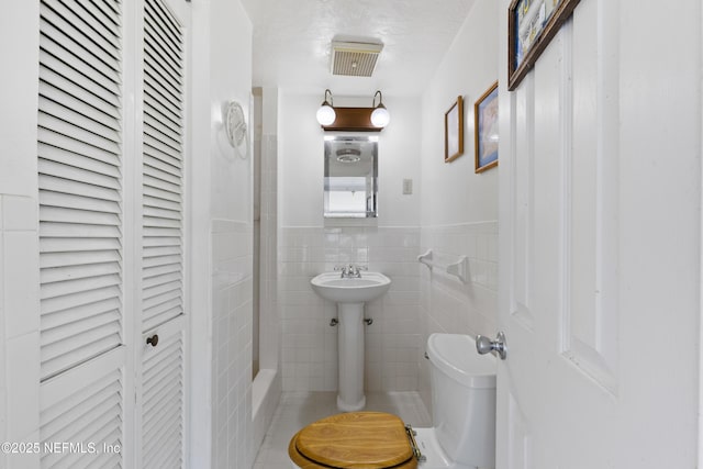 bathroom featuring a wainscoted wall, visible vents, toilet, tile walls, and a closet