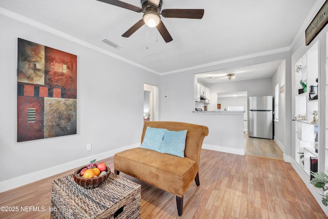 living area with baseboards, visible vents, ornamental molding, and light wood finished floors