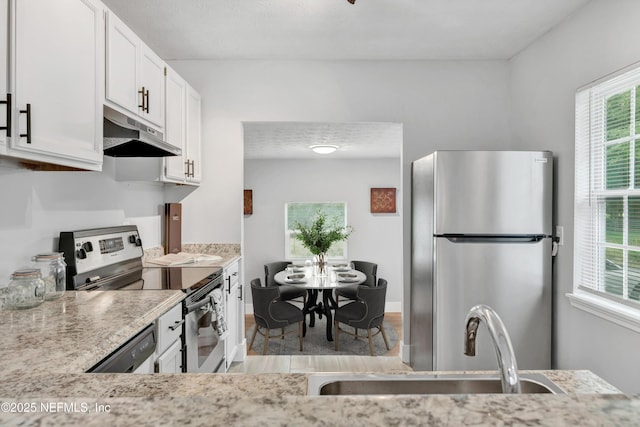 kitchen featuring light wood-type flooring, under cabinet range hood, white cabinets, a sink, and appliances with stainless steel finishes
