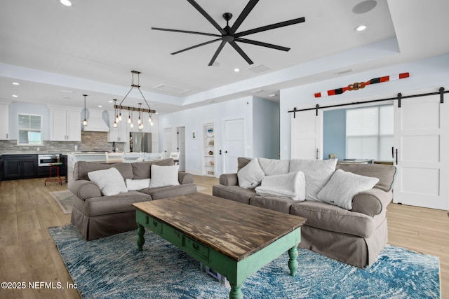 548 Sea Island Dr, Fernandina Beach, FL 32034 - living room with a barn door, a tray ceiling, light wood-type flooring, a ceiling fan, and recessed lighting