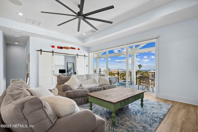 548 Sea Island Dr, Fernandina Beach, FL 32034 - living room with a barn door, ceiling fan, light wood-style floors, recessed lighting, and a tray ceiling
